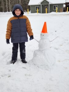 Lake Superior Academy student smiles for a picture with a snowman on the school grounds