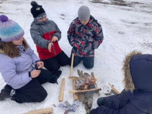 Lake Superior Academy students pose for a picture around a small campfire with their teacher in the school-yard.